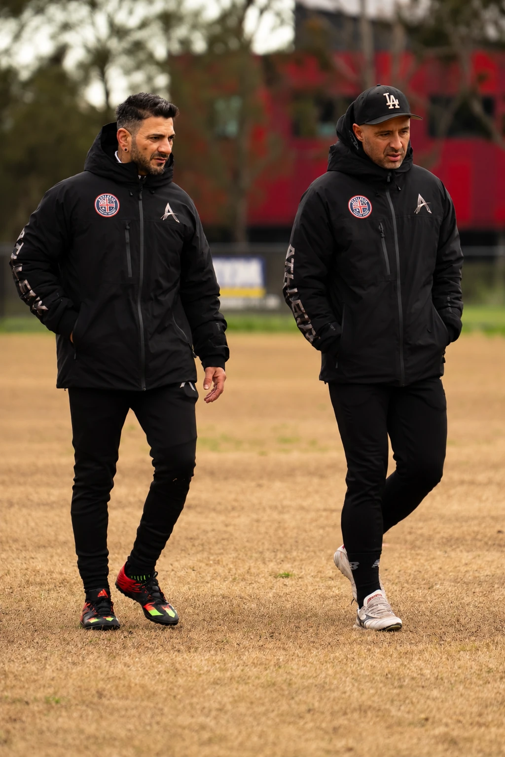 Two ATHLETIX coaches walking together on the football pitch